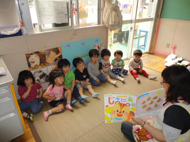 保育士が子どもたちに絵本の読み聞かせをしているところ。