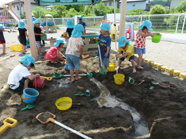 子どもたちが、砂場で川を作り、泥んこ遊びをしているところ