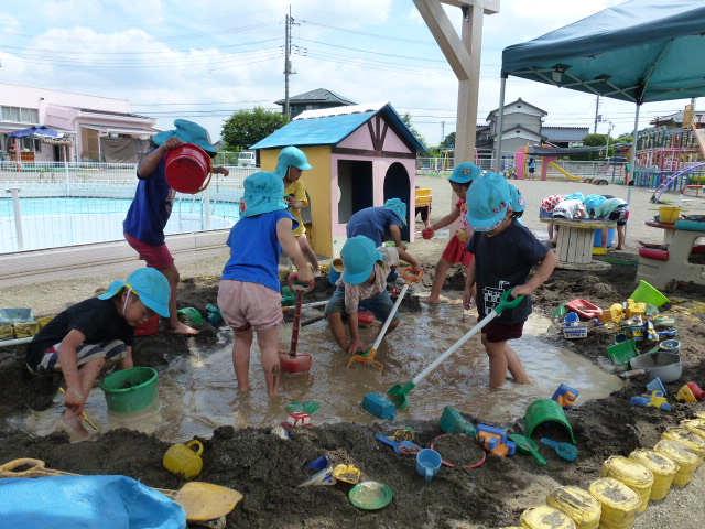 子どもたちが、砂場で水たまりを作り泥んこ遊びをしているところ