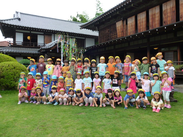 高麗郷古民家と七夕の笹飾りの前で、子どもたちが集合写真を撮っているところ