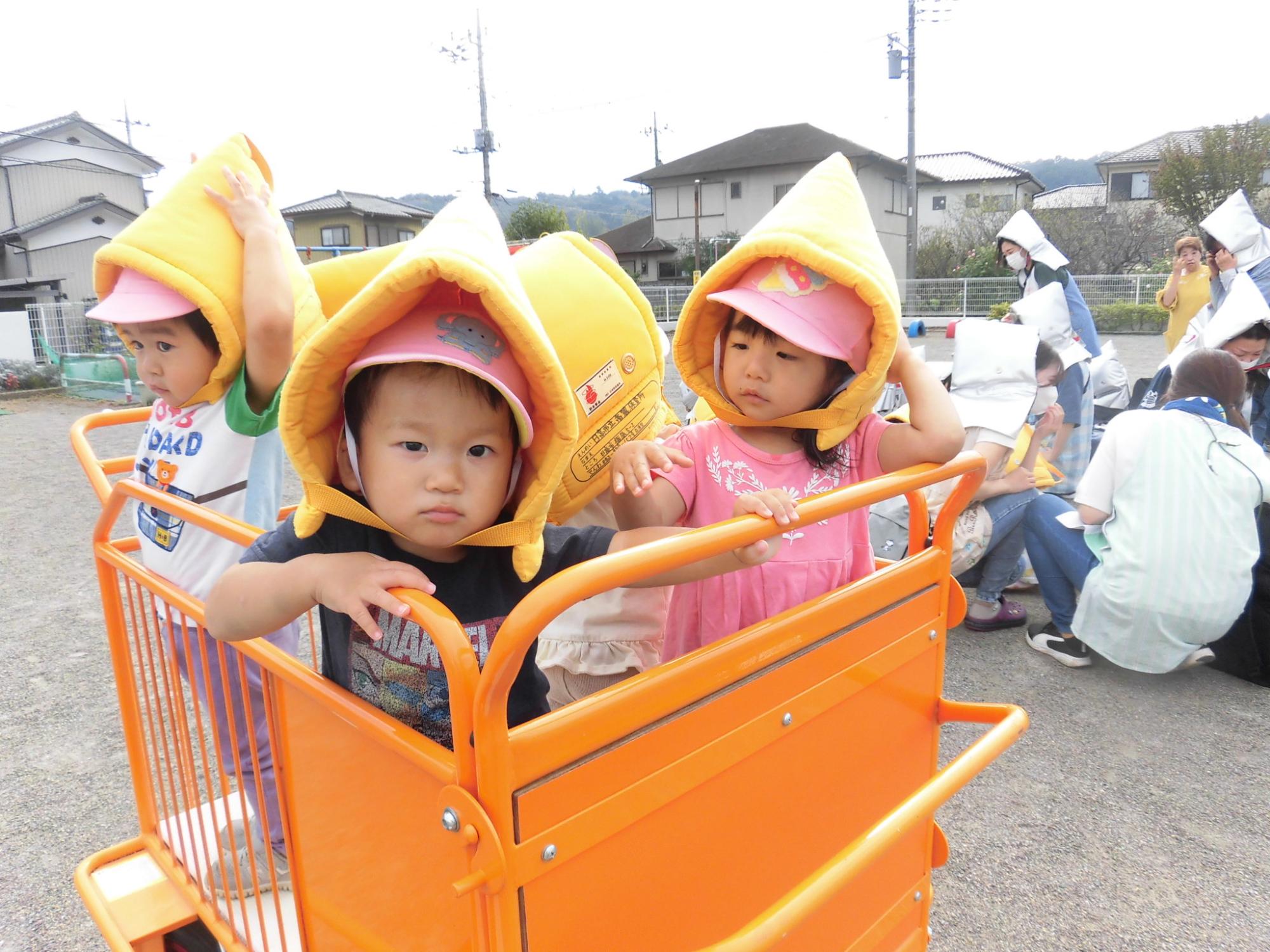 一歳児ももぐみの子どもたちが防災頭巾をかぶり、避難車に乗っているところ。