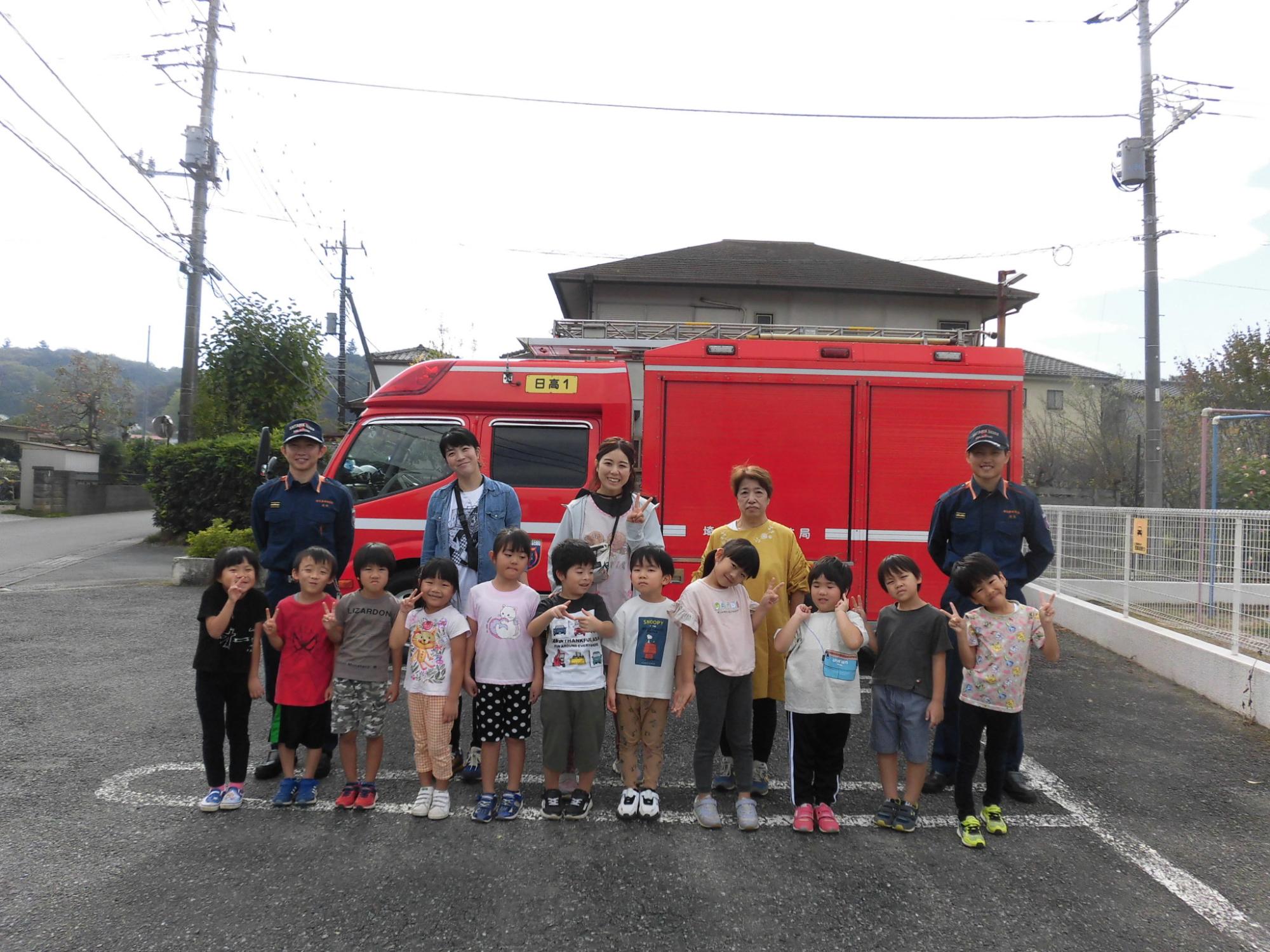 年長児ひまわりぐみの子どもたちが消防車の前で消防士さんと記念写真を撮っているところ。