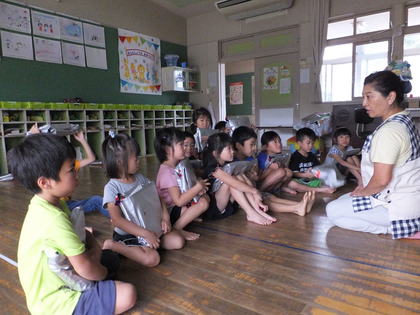 防災頭巾を持ち、保育士の話を聞く子どもたち