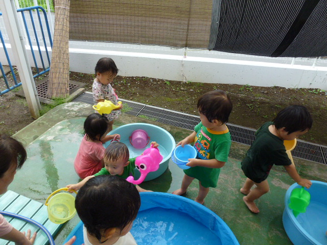 たらいに入った水で子どもたちがバケツやジョウロを使って遊んでいるところ。