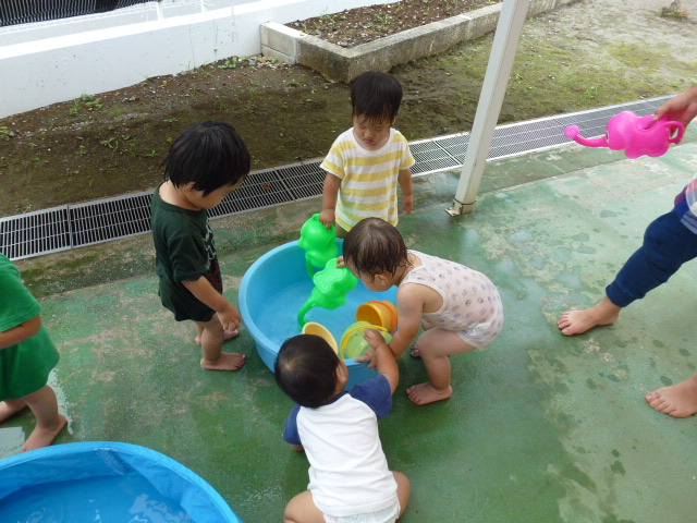 みんなでたらいを囲んでバケツやジョウロで水遊びをしているところ。
