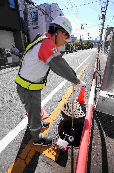 調査員が作業している写真です。道路上のマンホールを開け、測定機器を設置しています。