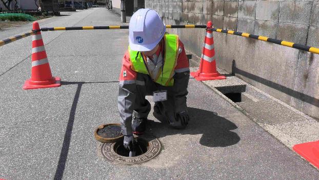 調査員が作業している写真です。道路上の鉄蓋を開けて作業しています。