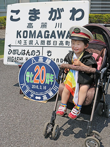 ベビーカーに乗っている笑顔の男の子。八高線電化20周年の際に日高町の時に使っていた高麗川駅のプレートが展示されている。