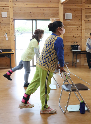 くりくり元気体操で足首におもりをつけて、椅子の後ろにたち足を横にあげる動き