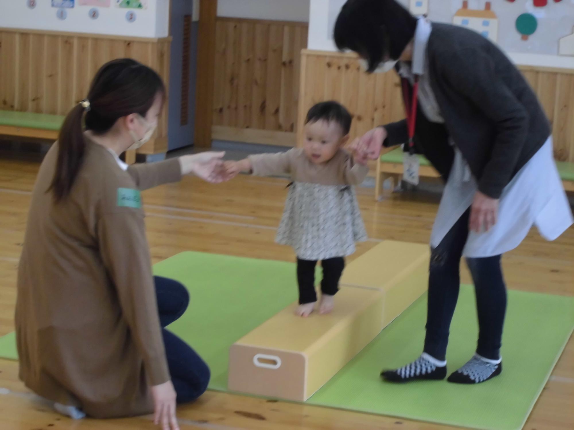 親の手を取り平均台を渡る子ども