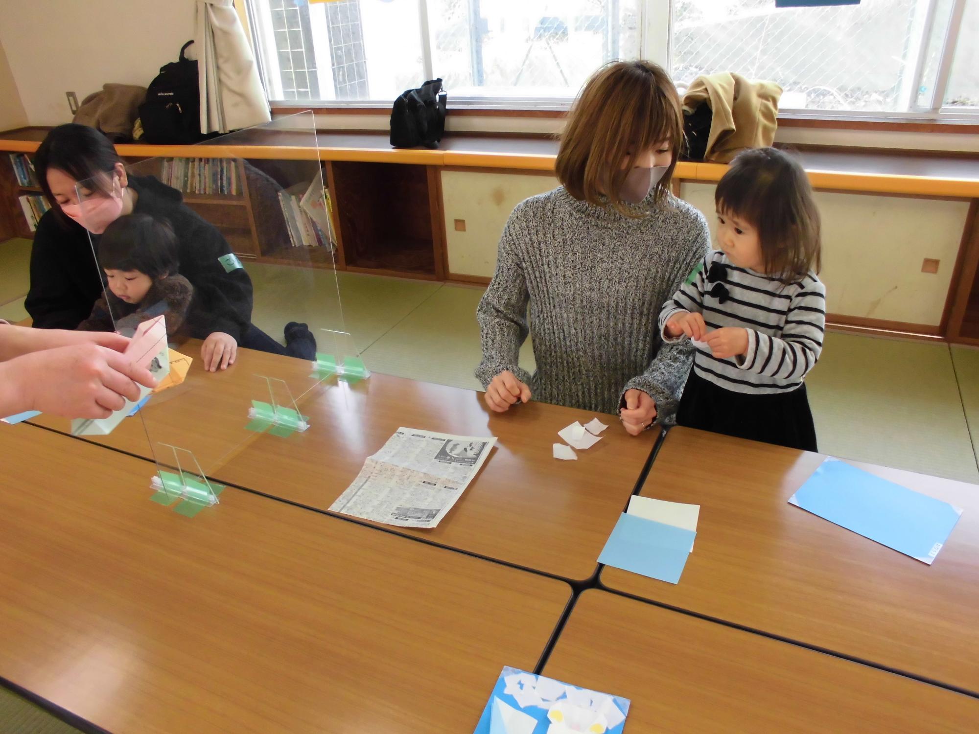 おりがみをちぎる子どもと見守る母親