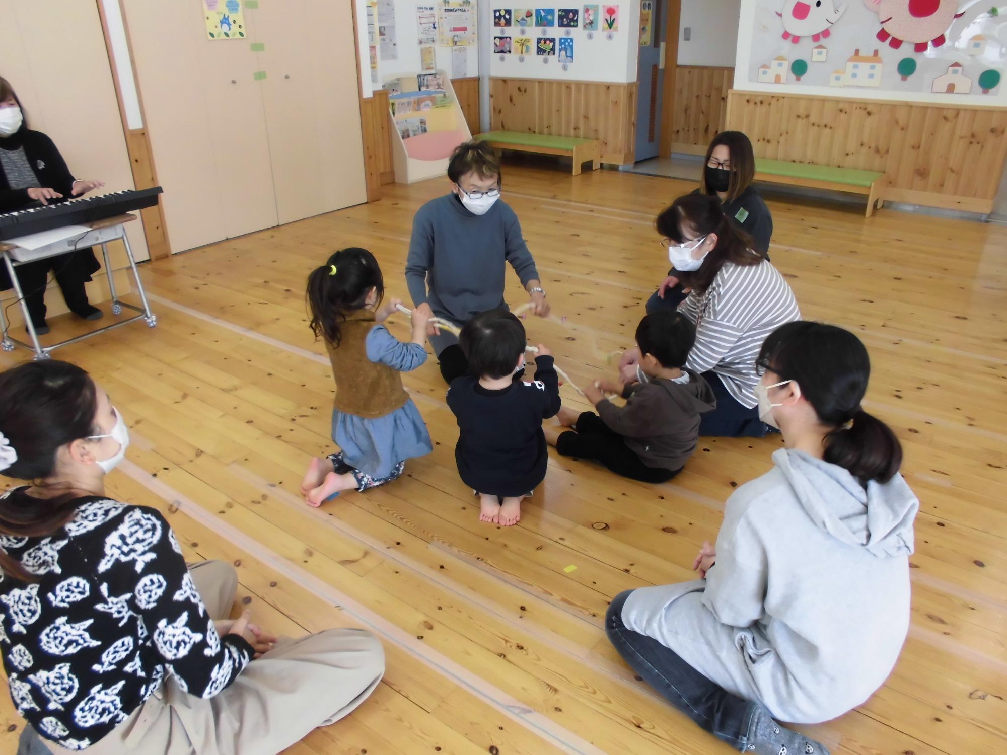 輪になり鈴のついたロープを握る子どもたち