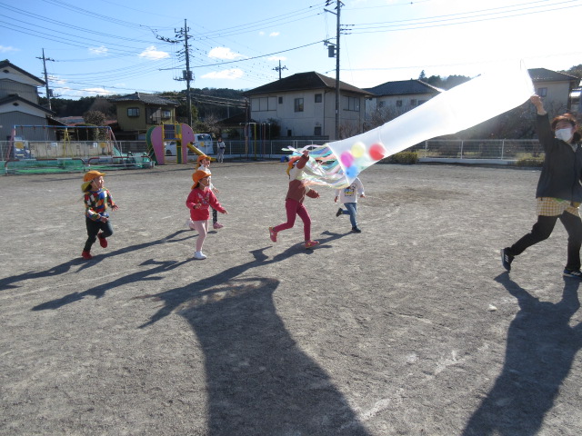 こいのぼりのような筒状の袋を職員が持って走り、子どもたちが追いかけている