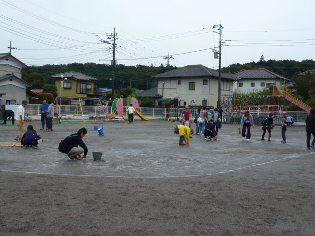 運動会。保護者の方々と保育士がぬかるんだグラウンドを整備しているところ。