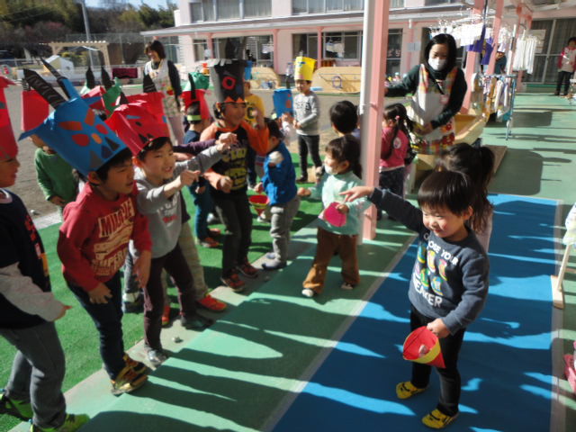 鬼のお面を付けている年長児に2歳児が豆をまいている写真。