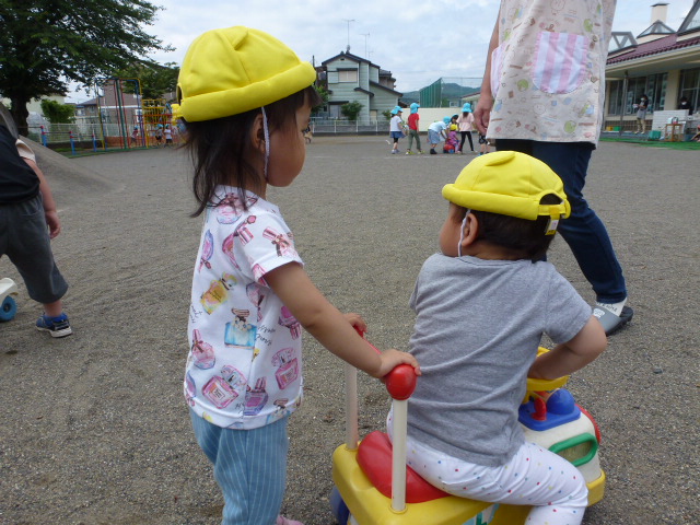 1歳児が乗るコンビカーの後ろを同じクラスの友達が押して遊んでいる。