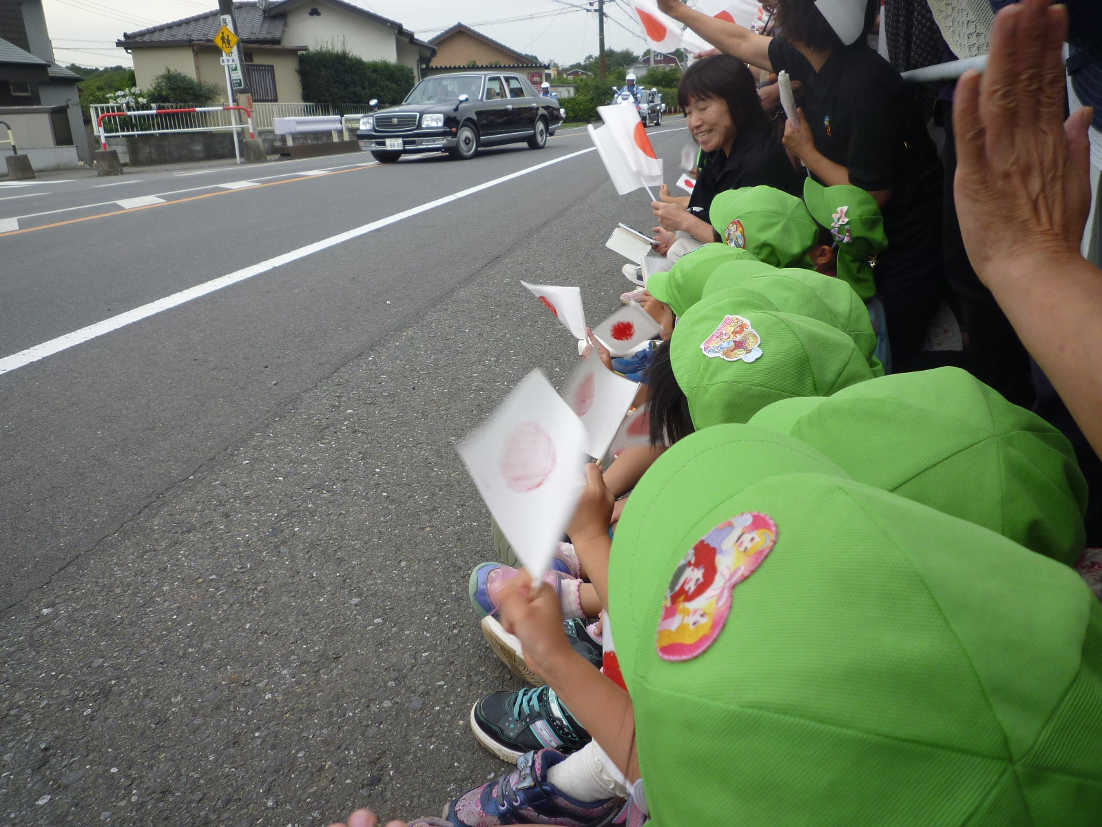 天皇皇后両陛下を乗せた車に日の丸の旗を振る子どもたち