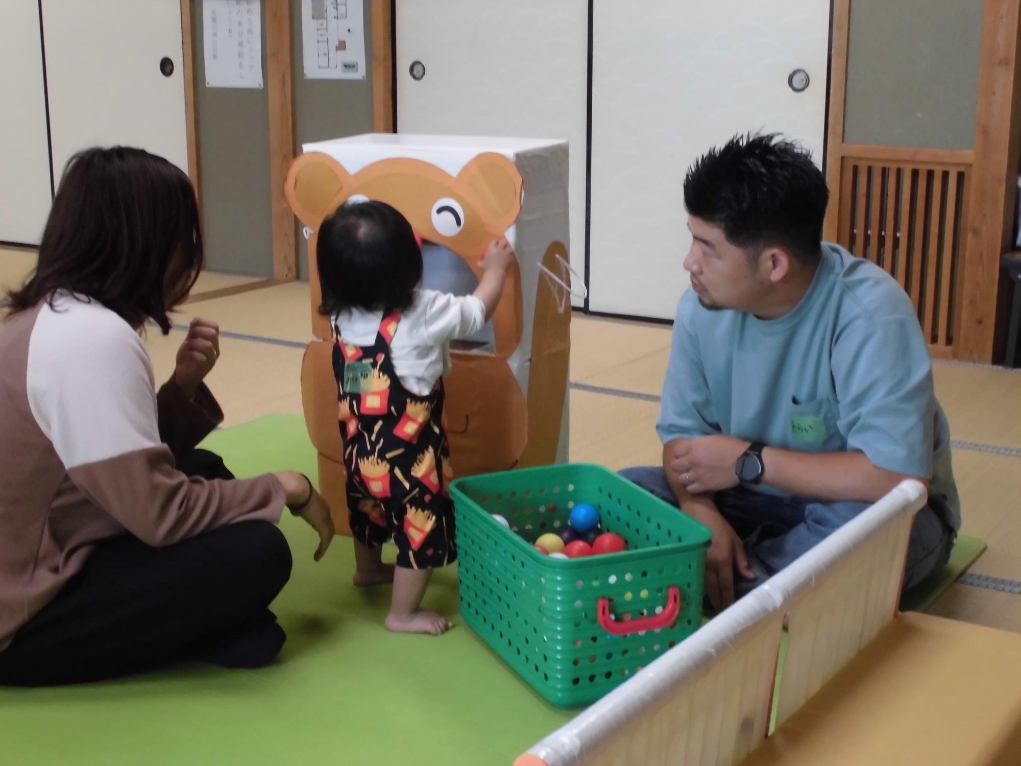 ダンボールでできたくまさんの口にボールを入れる子ども