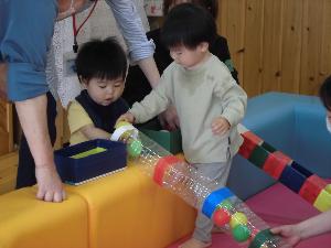 小さなボールをペットボトルのトンネルへ入れる子ども