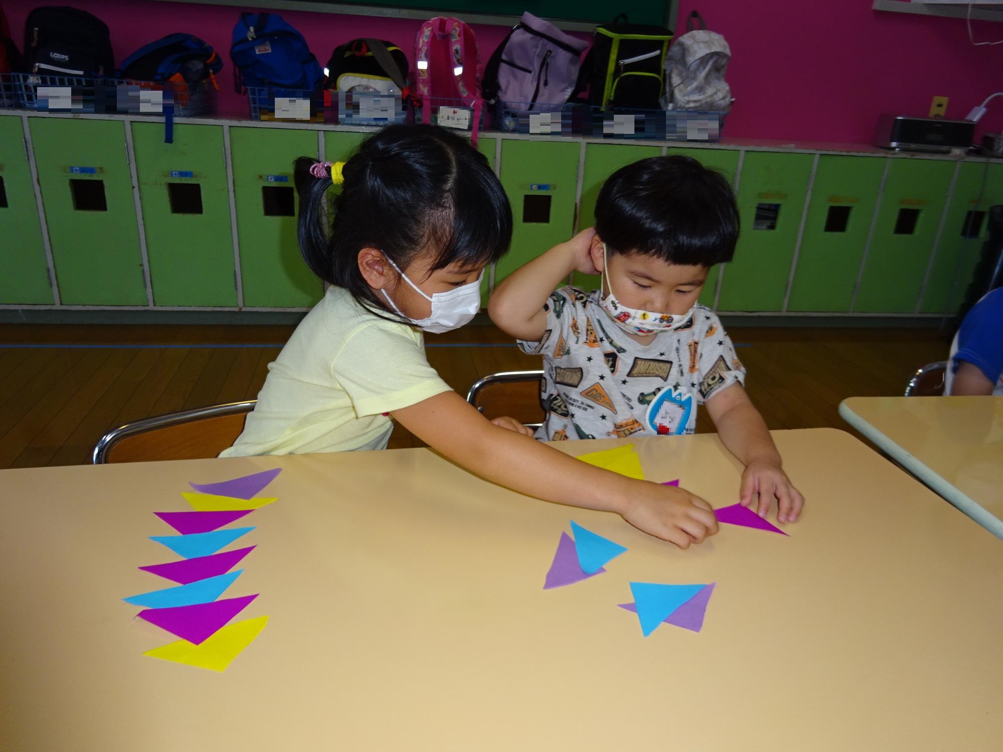 お姉さんが小さい子に折り紙の貼り方を教えているところ