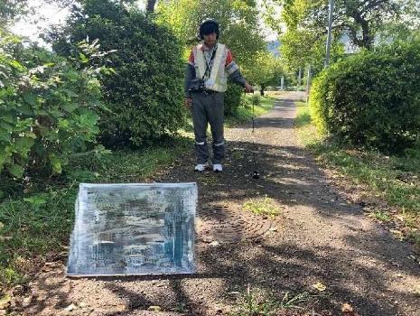 道路に埋設されている水道管を調査している写真です。調査員はヘッドホンをつけ、路面に機器をあてながら歩いて調査しています。