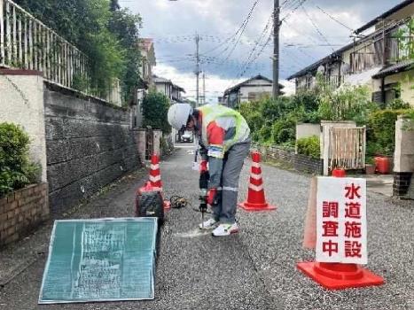 道路に埋設されている水道管を調査するため、道路にドリルで穴を置けている写真です。調査時はカラーコーンや看板を設置して作業しています。