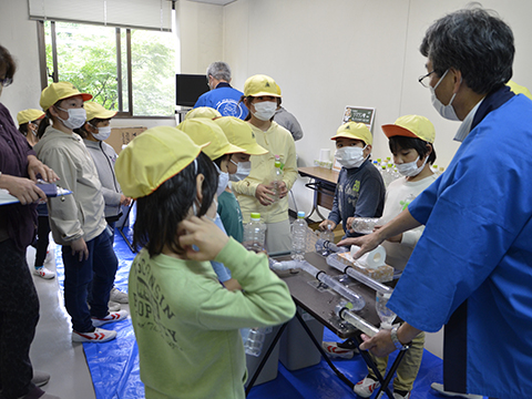 ティッシュとトイレットペーパーの管詰まりの違いを見る実験の説明を聞く小学生の様子