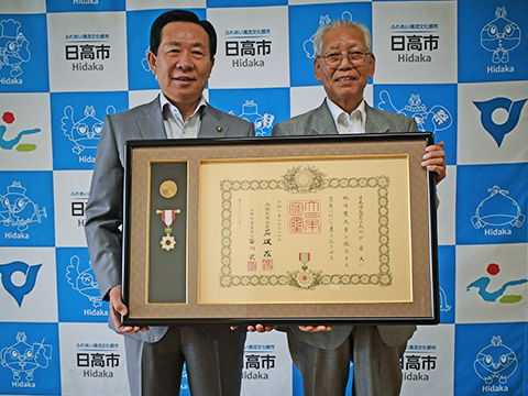 授与された賞状と勲章を市長とともに笑顔で持つ大川戸さん