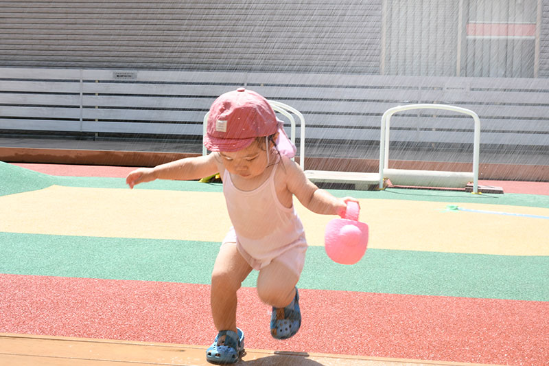 シャワーで水をかけてもらって水遊びを楽しむ子どもの様子
