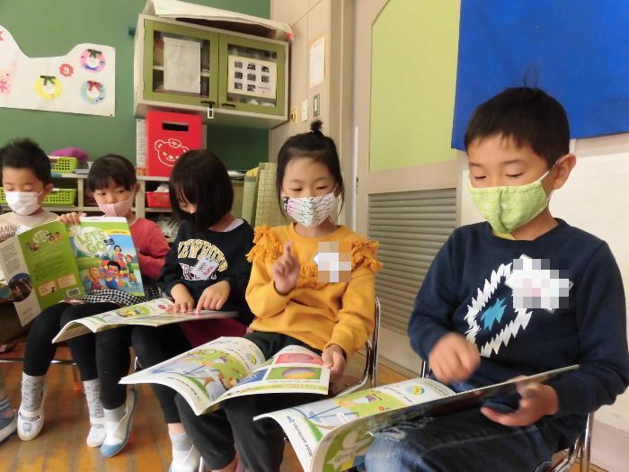 子供たちの大好きな遊びの歌をテキストを見ながら歌っている写真。
