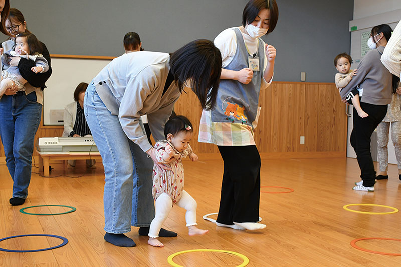 お母さんに支えられ、輪になって踊っている女の子