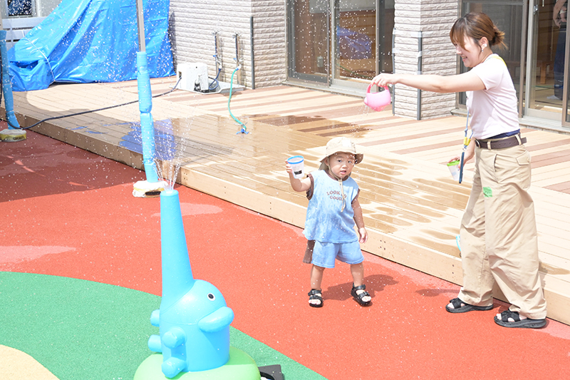ママと一緒にゾウさんの噴水の前で水のかけっこをしている様子