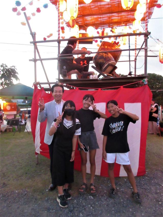 夏祭り会場で、来場者3名と笑顔で写真に映る谷ケ崎市長