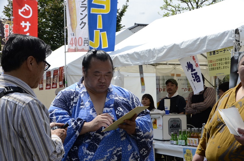 会場の外でサインを書く浴衣姿の力士