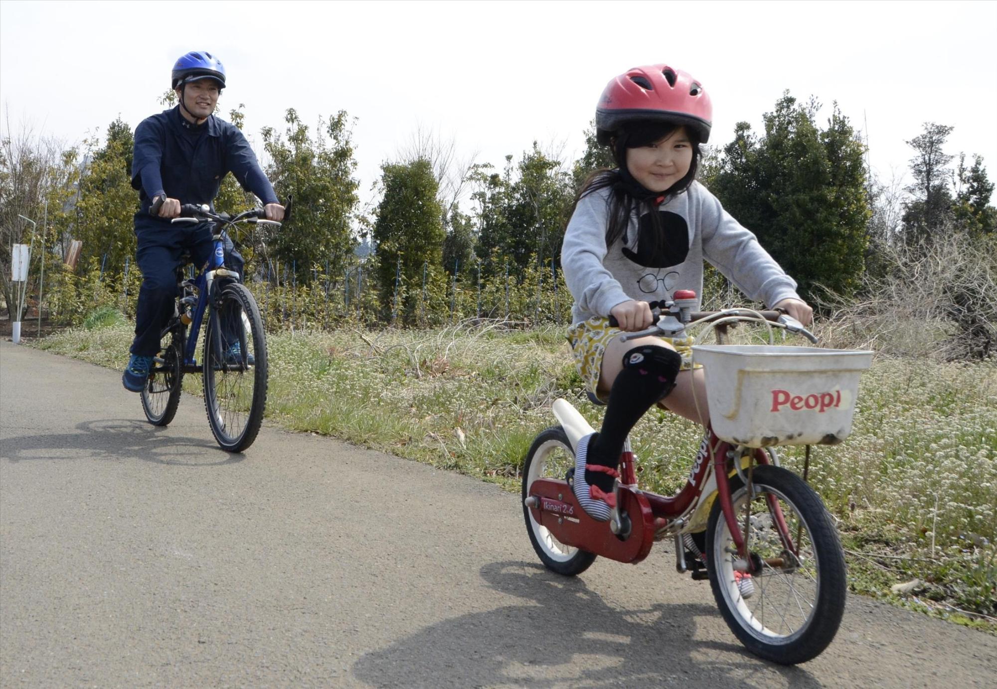 ヘルメットをかぶって自転車に乗る親子の写真