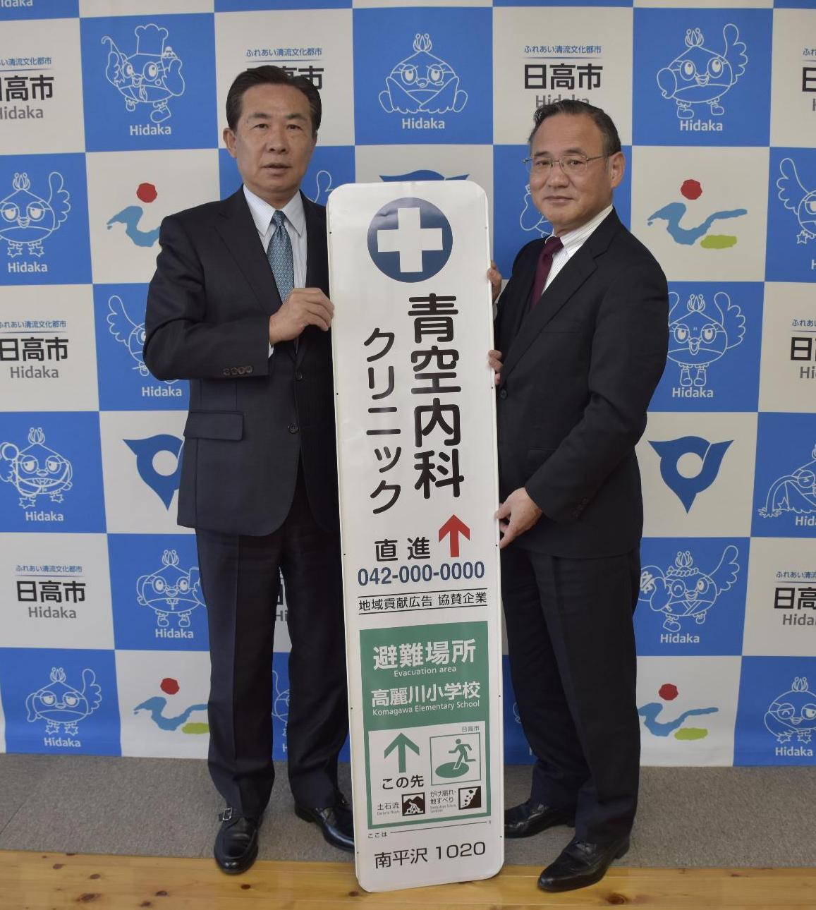 地域貢献型広告のサンプルを挟んで谷ケ崎市長（左側）と石川信次埼玉総支社長