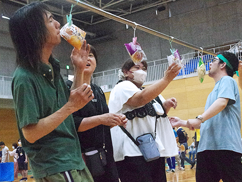 パン食い競争にてパンを咥えようと跳んでいる出場者