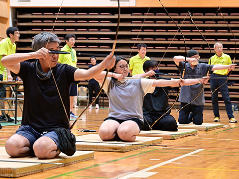 正座しながら横一列になり、矢をつがえ的を狙う参加者たち