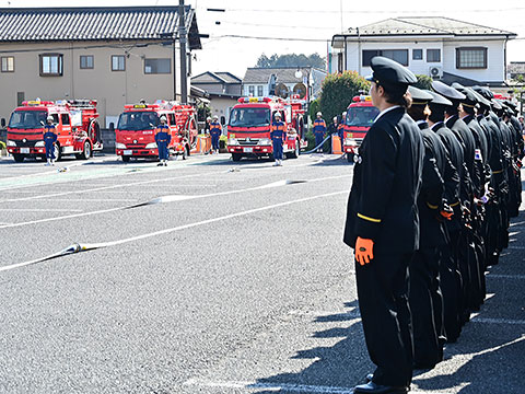 放水のため消防車前で準備する消防団員と見学している消防団員