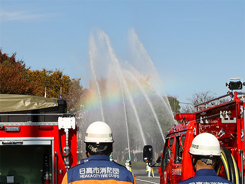 消防車の後ろから放水を見つめる消防団員