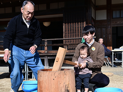大人に支えられながら臼で餅をつく子ども
