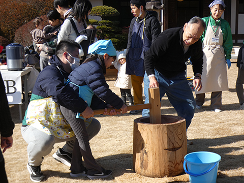 大人に支えられながら臼で餅をつく子ども