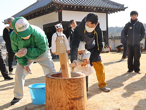 大人に支えられながら餅をつく子ども