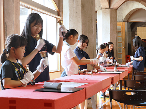 聖望学園高等学校の生徒たちからハンドベルの演奏の仕かたを教わる子どもたち