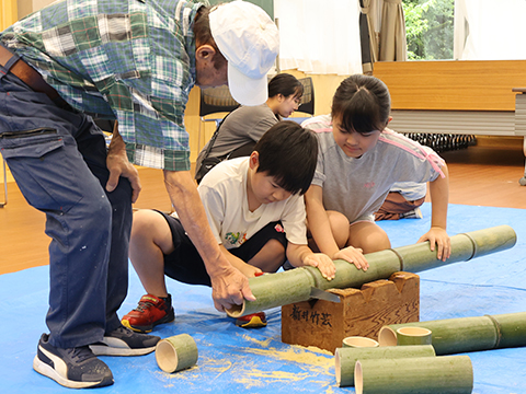 地域の人に教わりながらのこぎりで竹を切っている子どもたち